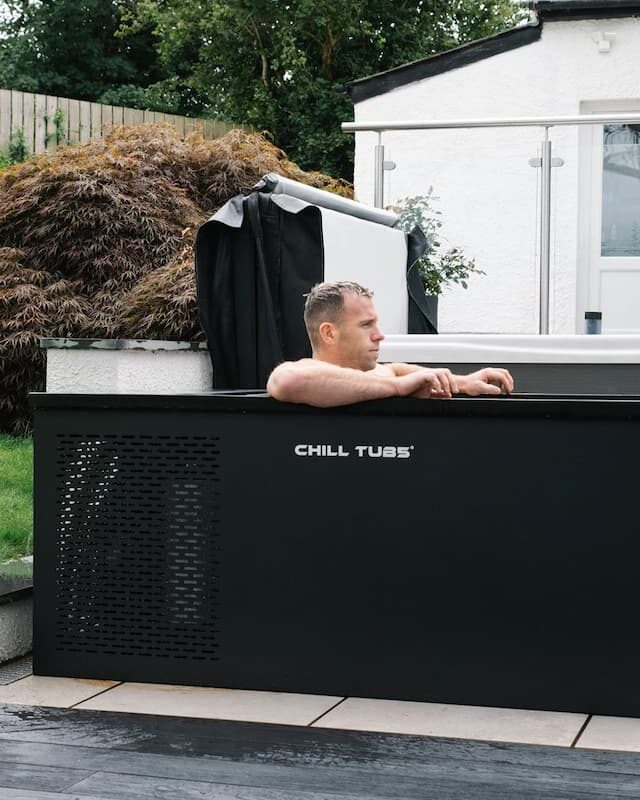 Gareth Davies sitting in a Chill Tub ice bath outside in a garden.